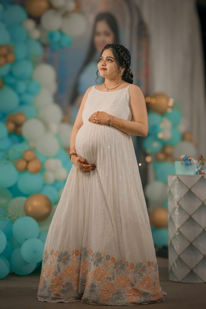 Graceful pregnant woman poses elegantly at an indoor celebration with a blue balloon decor in India.